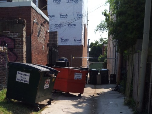 Conditions in an H Street alley last summer.  The fence has been removed but trucks displaced by street cars must use the alley for deliveries to H Street restaurants.
